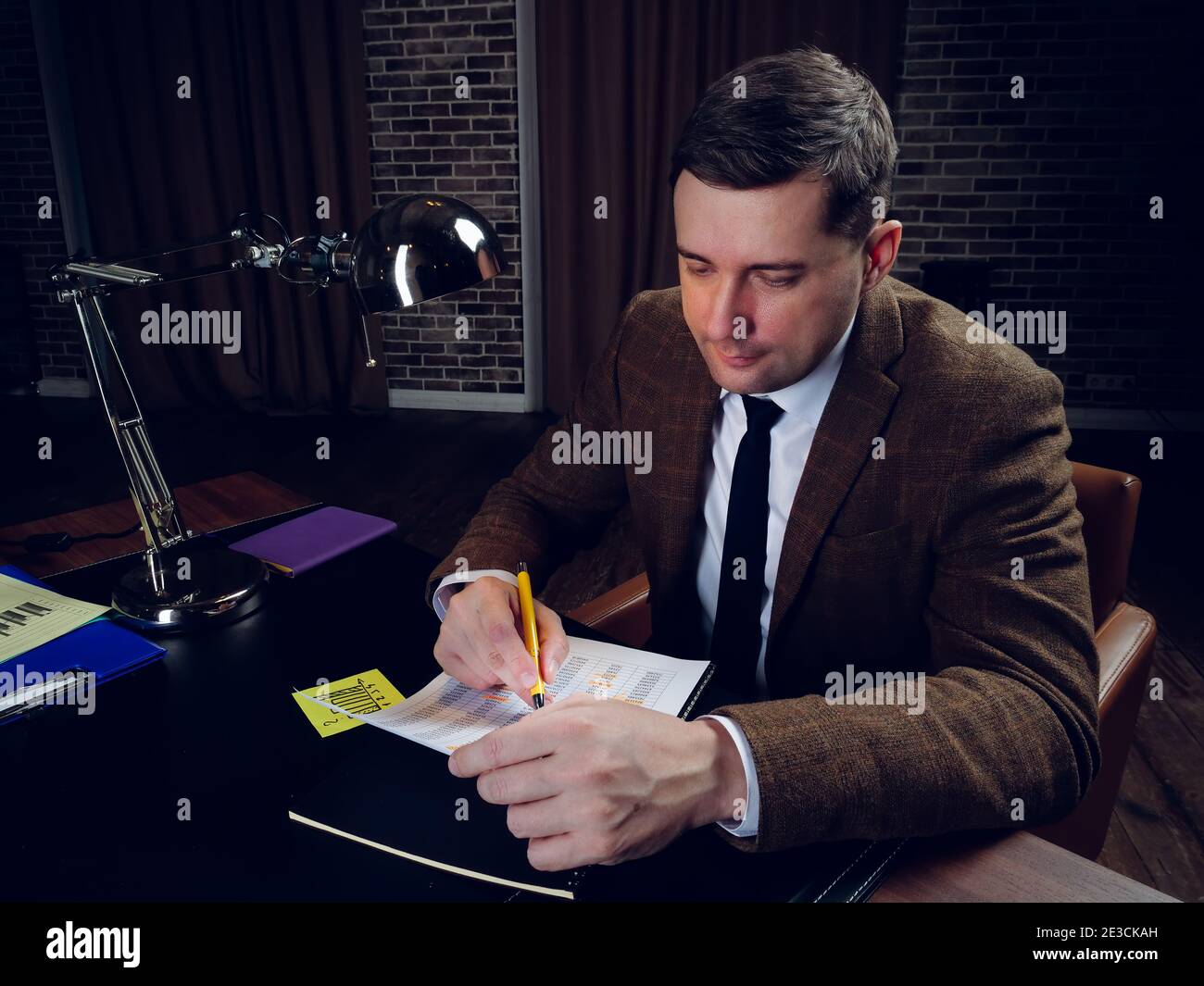 Uomo d'affari in tarda notte lavora con i documenti mentre si siede al tavolo. Foto Stock