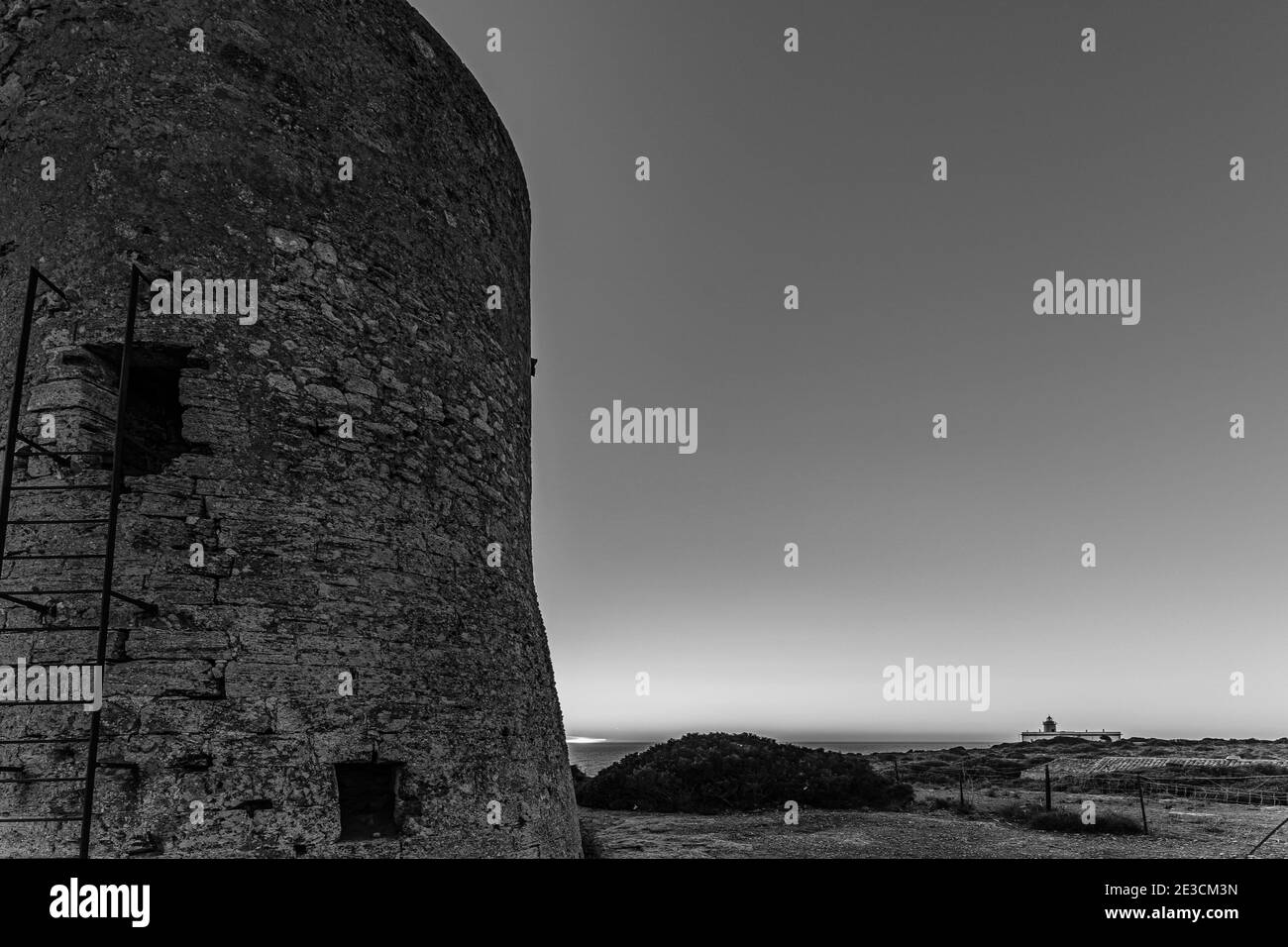 Torre di guardia Cap Blanc in bianco e nero a Maiorca con il faro sullo sfondo al tramonto. Questa torre costruita nel s. XVI avvertì del pirata. Foto Stock