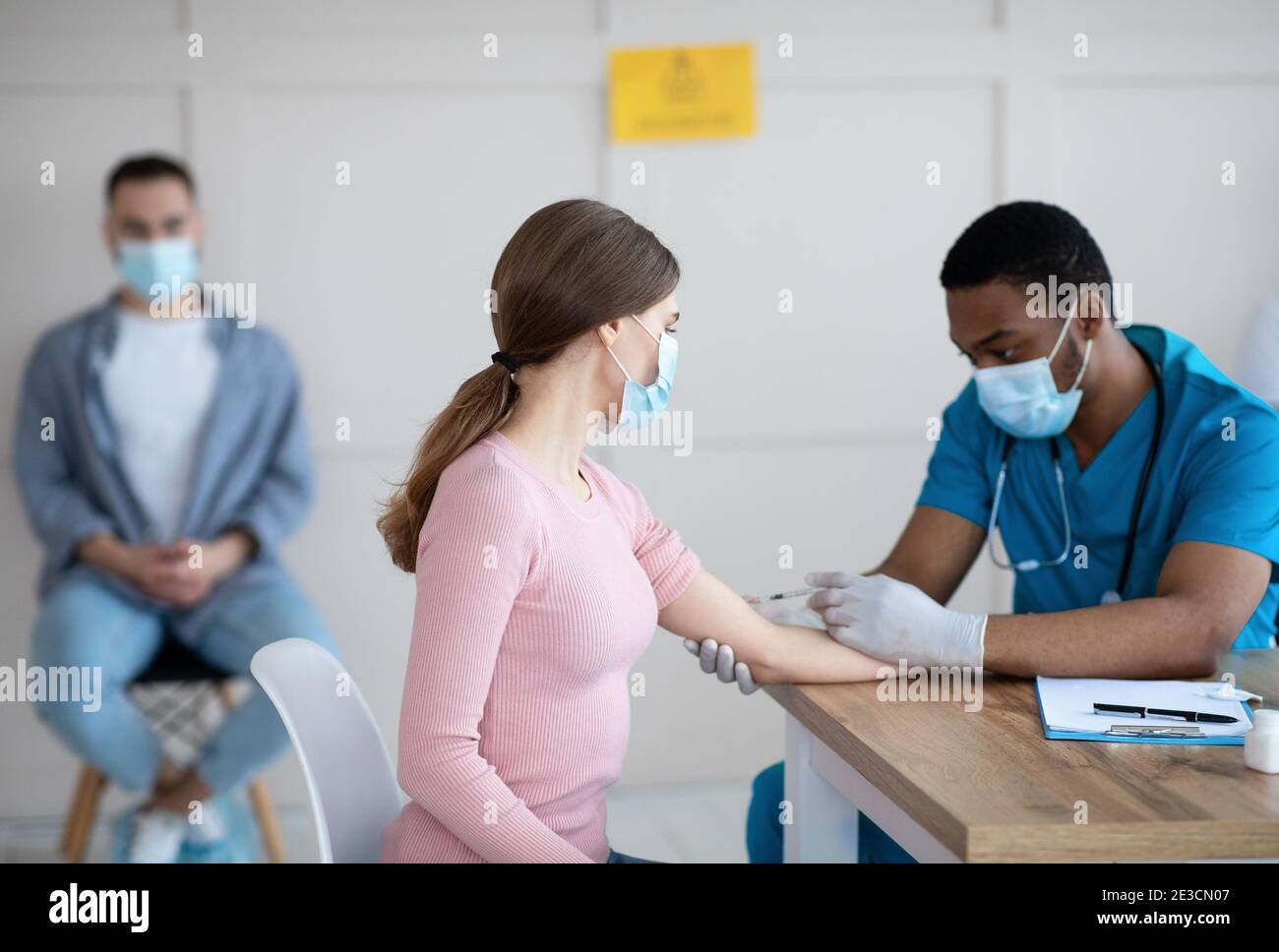 Medico afroamericano che inietta il vaccino covid-19 a una giovane donna in clinica. Immunizzazione contro il virus globale Foto Stock