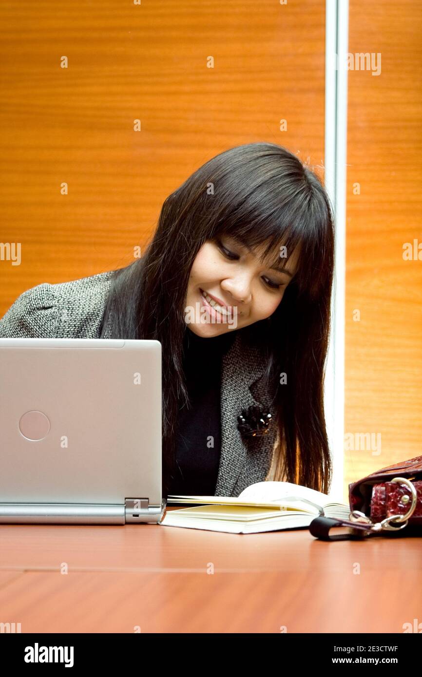 Felice donna asiatica che lavora in ufficio con notebook e agenda Foto Stock