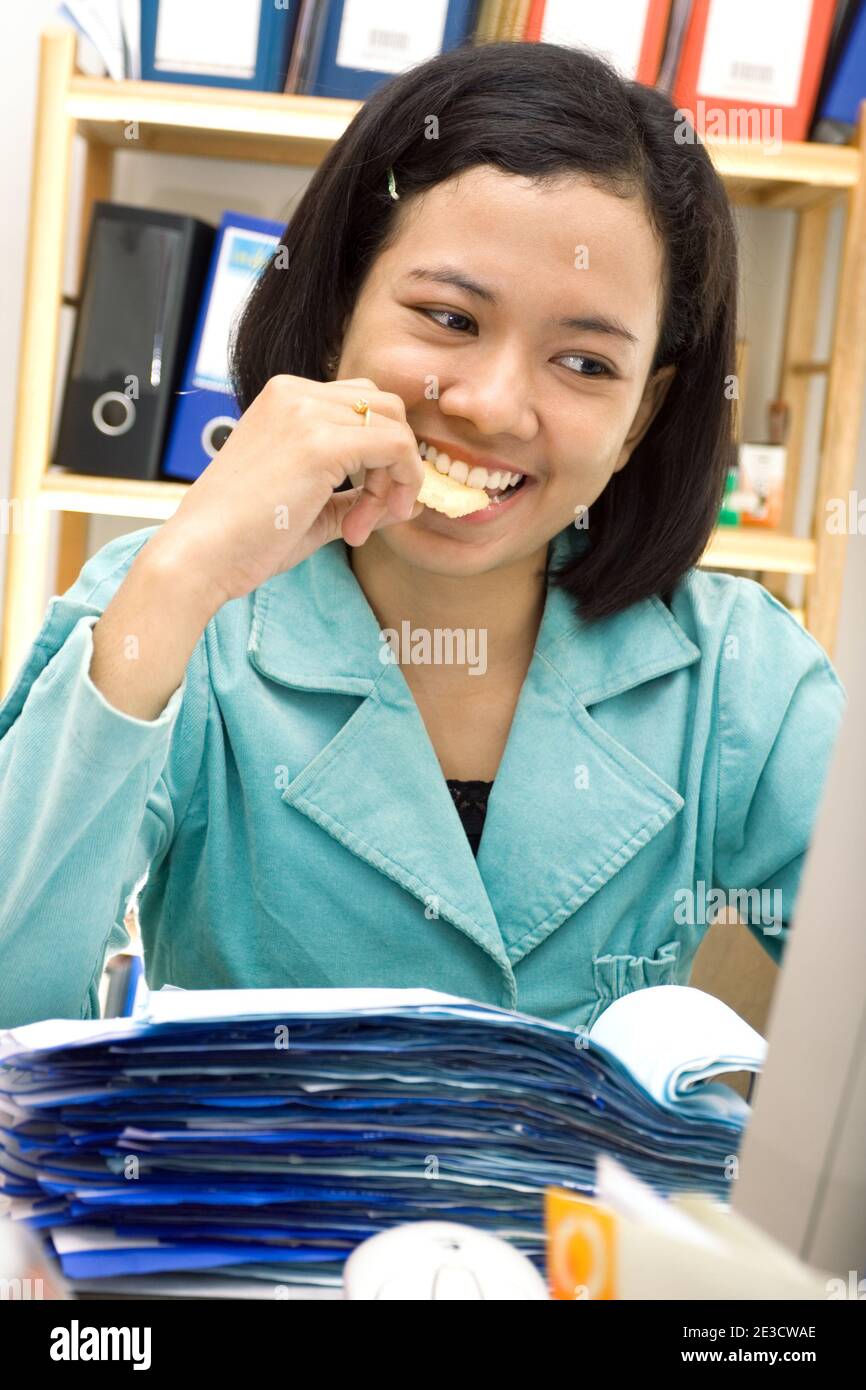 una donna asiatica che mangia snack mentre fa il suo lavoro Foto Stock