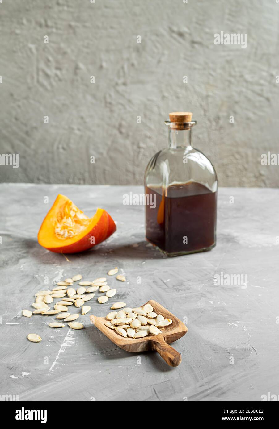 Una bottiglia di olio di semi di zucca, una fetta di zucca e semi di zucca in un cucchiaio di legno su sfondo grigio, foto verticale con spazio per la copia Foto Stock