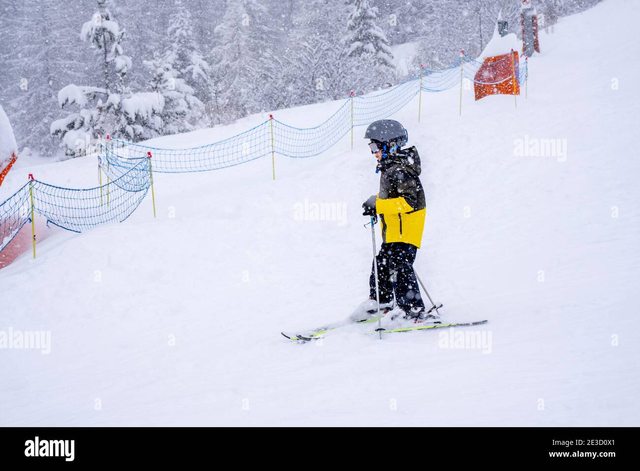 Sci per ragazzi in pendenza, fai una lezione di sci durante una giornata di nevicate, neve fresca sulla foresta durante una nevicata. Sci da giovane in maschera e casco su s. Foto Stock