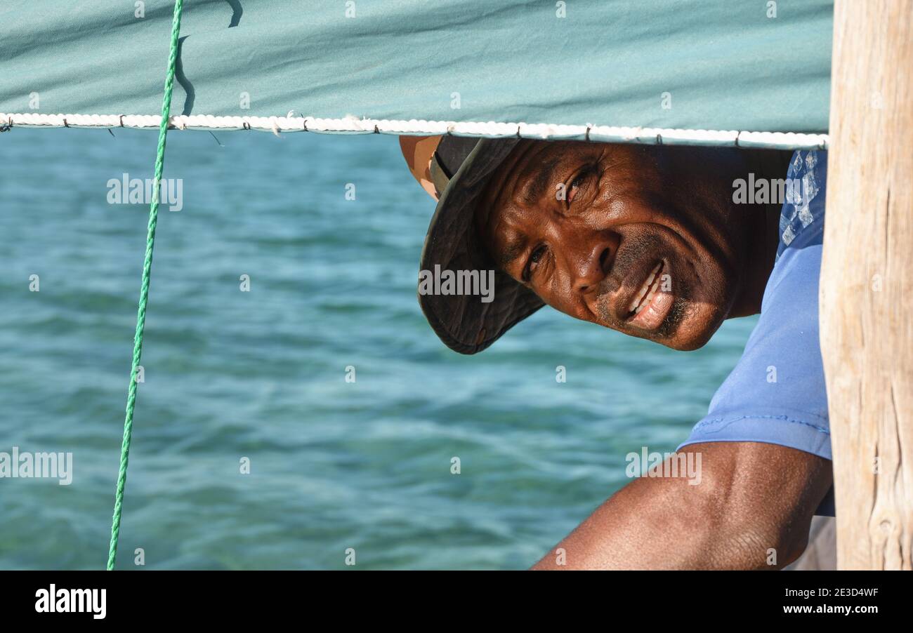 Anakao, Madagascar - 03 maggio 2019: Sconosciuto pescatore malgascio guardando indietro sotto la principale vela verde della sua piroga (piccola barca da pesca), verde blu mare du Foto Stock