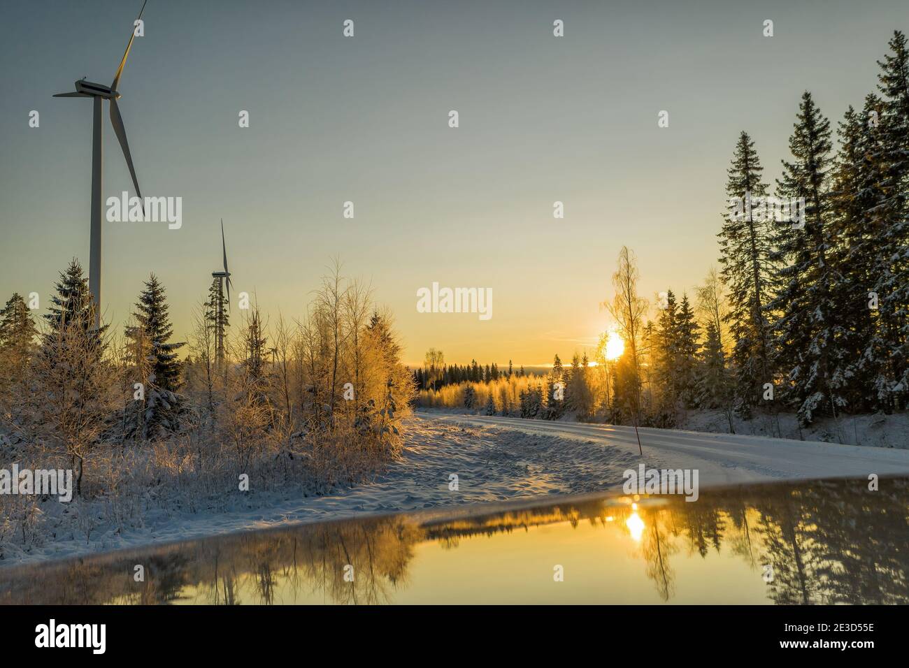 Bella inverno dorato Tramonto nella foresta scandinava vicino a due turbine eoliche riflesse in molto pulito tetto di auto lucido. Strada di campagna invernale. Sole behi Foto Stock