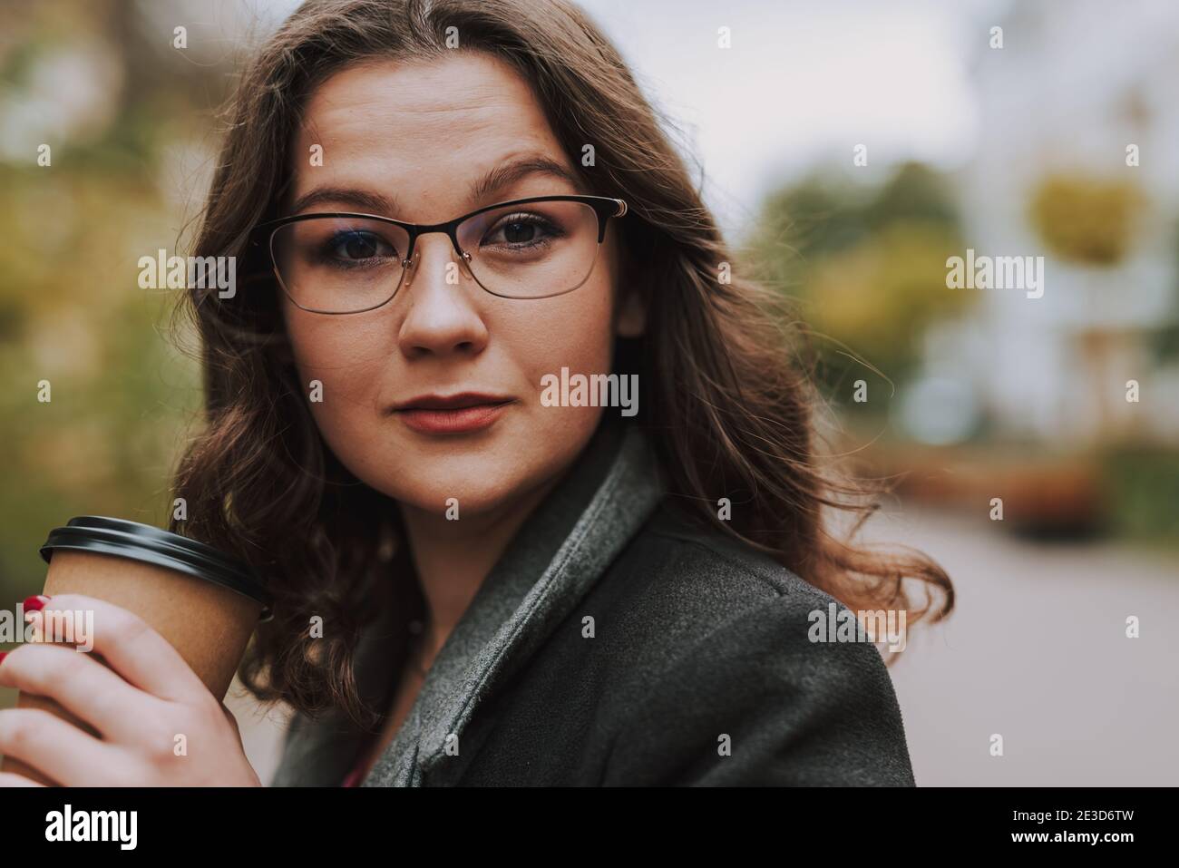 Ritratto di bella giovane donna in spectacled nella tenuta di strada una tazza di caffè in movimento Foto Stock