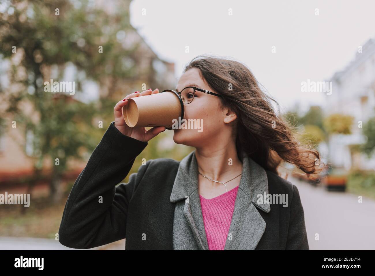 Giovane donna attraente che beve il caffè da una tazza di carta e. guardando via Foto Stock