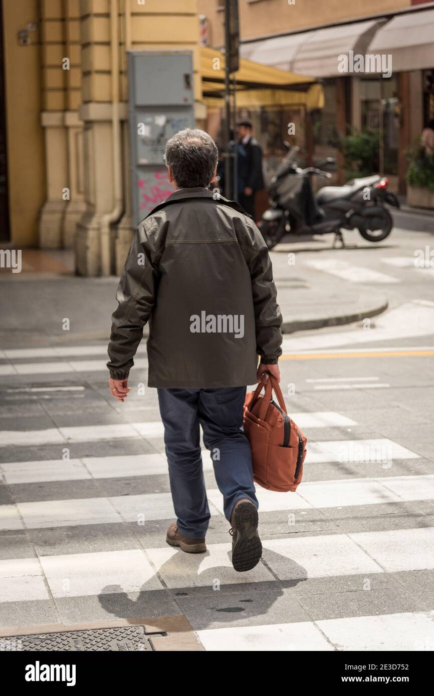 Un uomo di mezza età in un cappotto di pelle che attraversa un pedone Al sole a Bologna italia Foto Stock