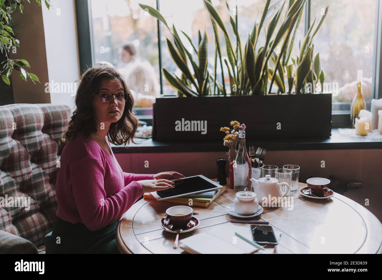 Donna sorridente e attraente che si siede al bar mentre lavora con il digitale tablet e tè Foto Stock