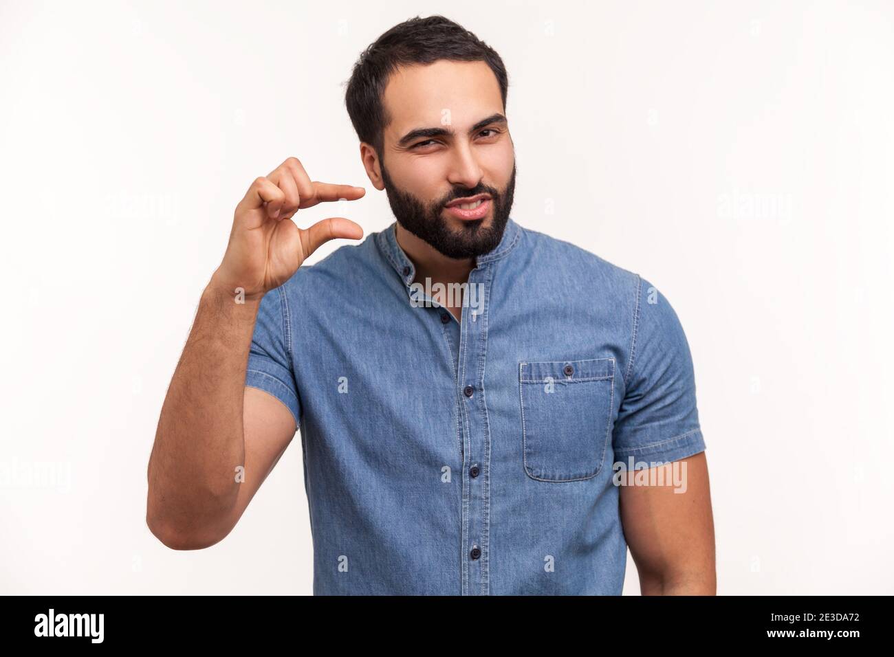 L'uomo infelice bearded che osserva deluso e che mostra un piccolo gesto della punta, piccola quantità o segno della scala bassa, alcuni centimetri. Isolamento delle riprese in studio al coperto Foto Stock