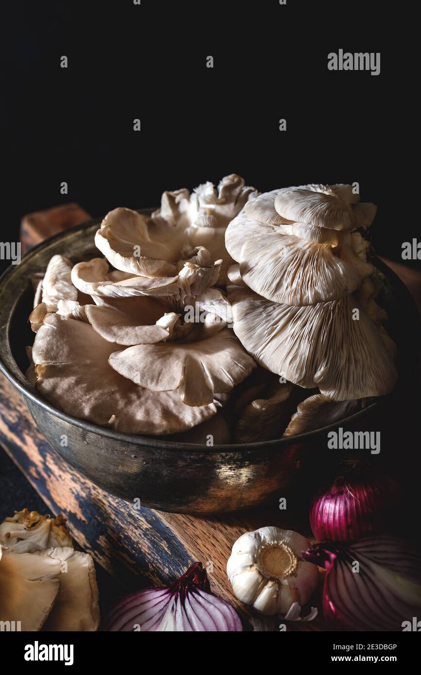 Funghi di ostrica in una vecchia pentola con verdure su sfondo scuro. Primo piano. Foto Stock