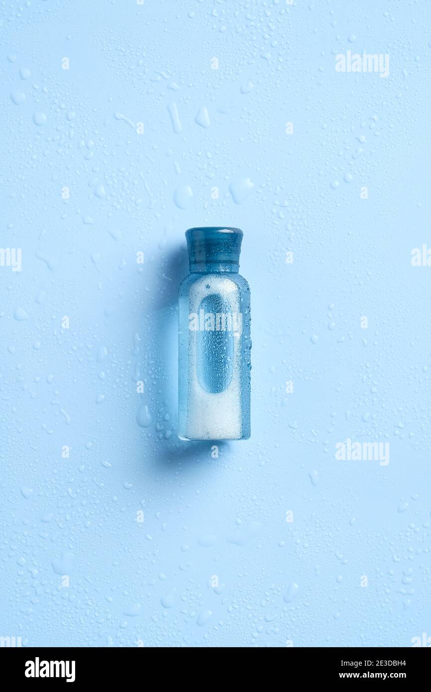 Bottiglia cosmetica bagnata su sfondo blu vista dall'alto. Design di confezionamento del prodotto di bellezza idratazione, mockup di contenitori cosmetici Foto Stock