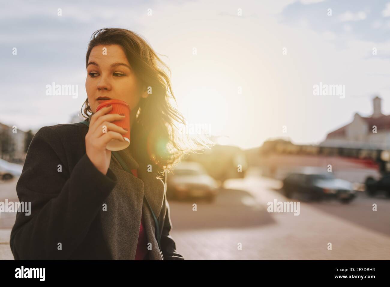 Vita in su di giovane donna attraente in piedi sulla strada mentre tenete il caffè e guardate via Foto Stock