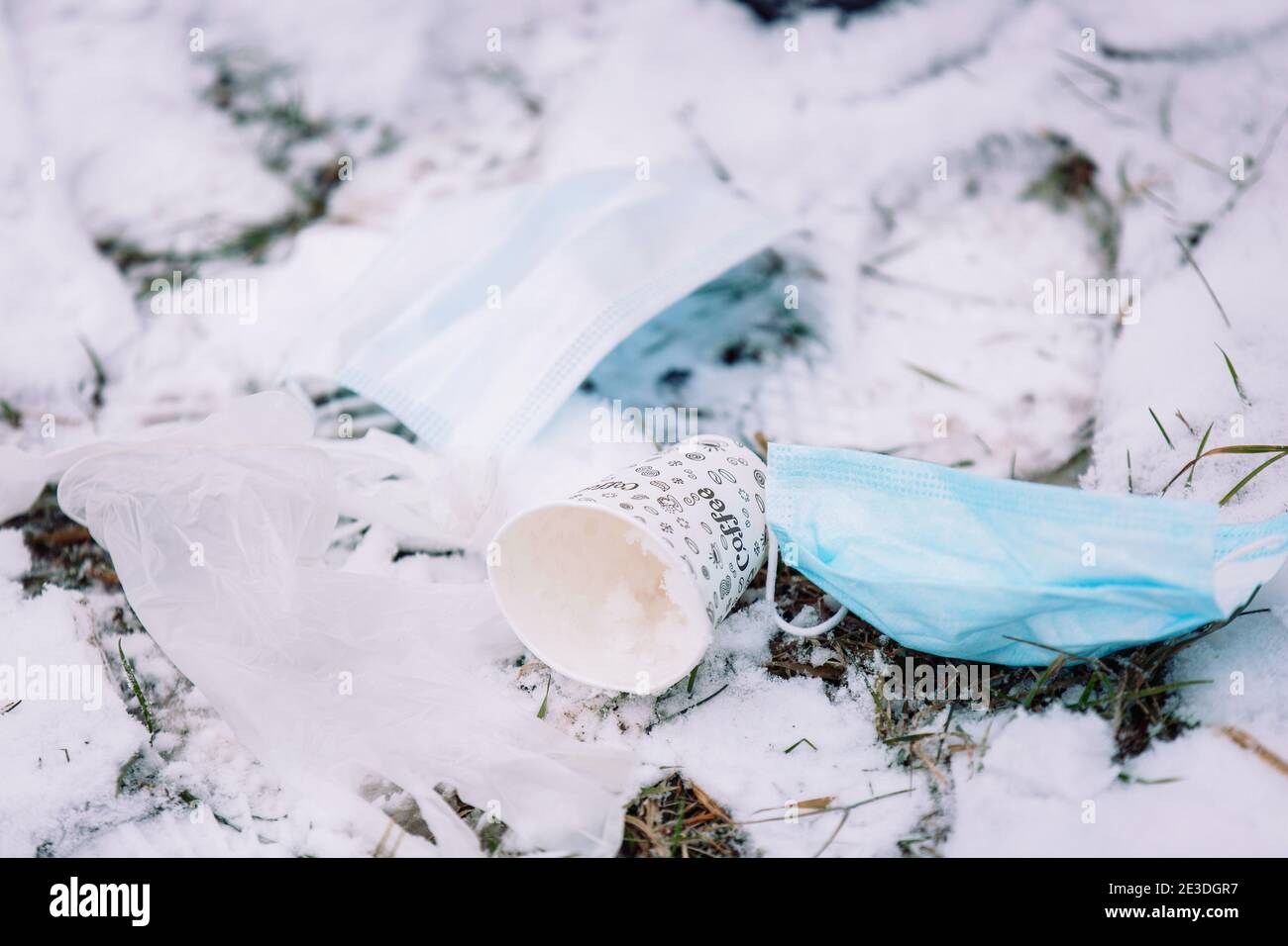 I rifiuti provenienti dalla pandemia contaminano la terra. Maschere monouso per uso medico, guanti medici e una tazza di plastica, gettati sul terreno nevoso nel Foto Stock