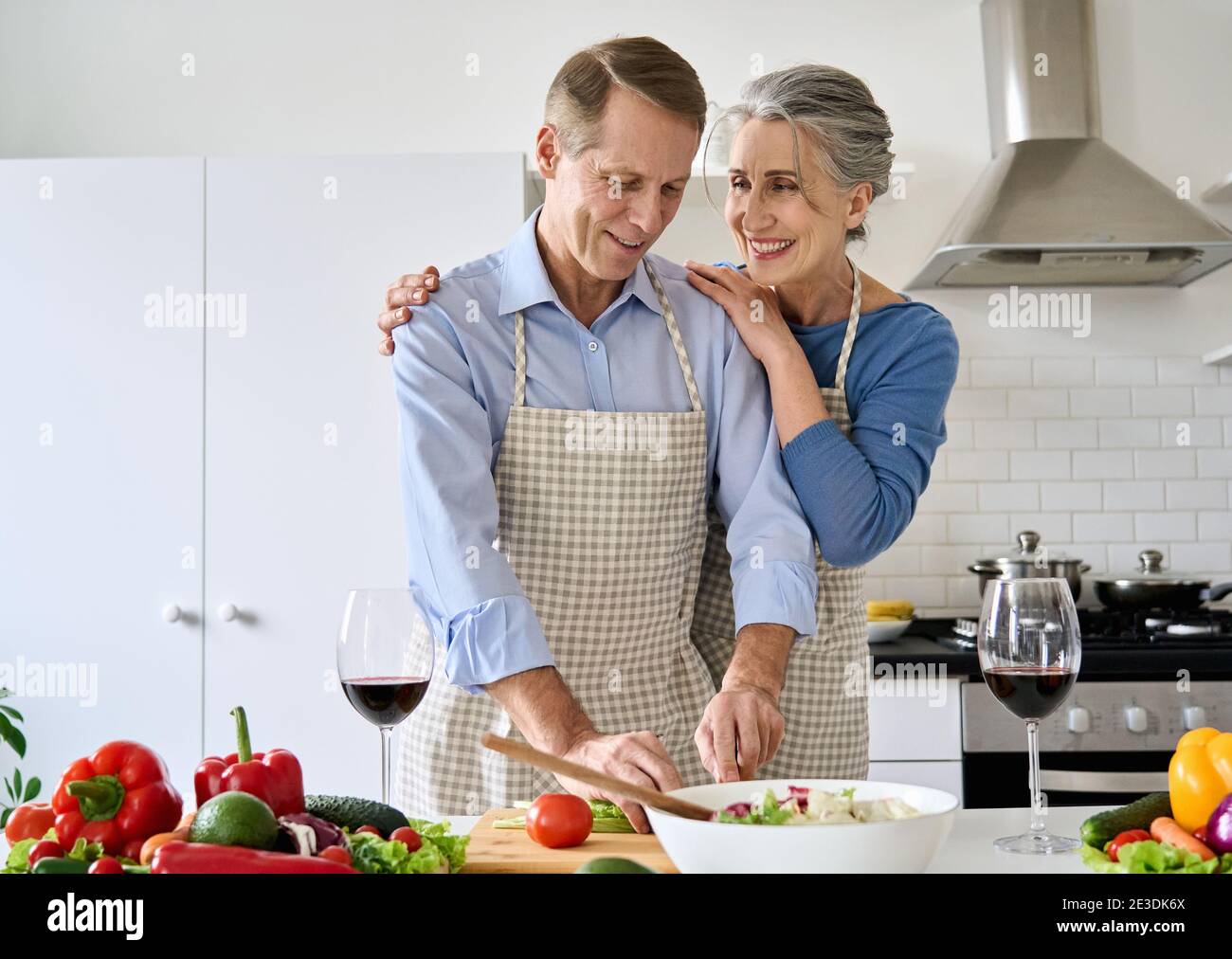 Felice anziano coppia bere vino preparare dieta sana insalata abbracciare a casa. Foto Stock