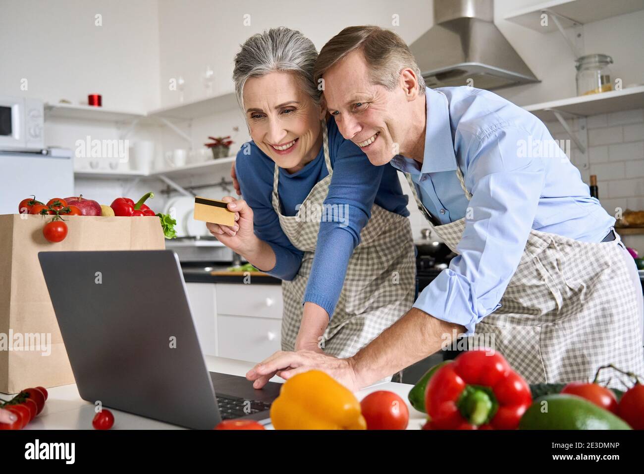 Felice vecchia coppia usando il laptop che tiene la carta di credito ordinare cibo nella drogheria online. Foto Stock