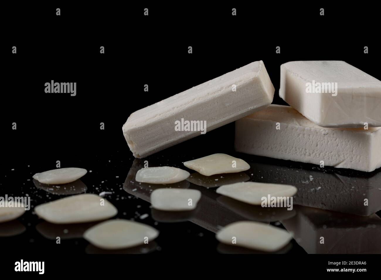 le barrette bianche di sapone sono impilate una sull'altra con i residui di sapone e i pezzi che si trovano intorno sulla superficie scura riflettente. Un'immagine concettuale per Foto Stock