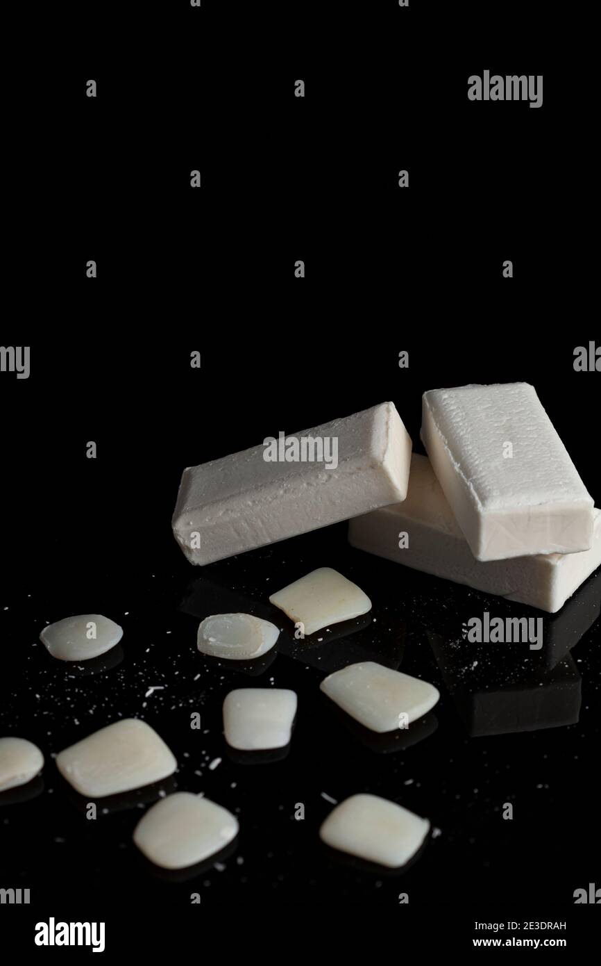 le barrette bianche di sapone sono impilate una sull'altra con i residui di sapone e i pezzi che si trovano intorno sulla superficie scura riflettente. Un'immagine concettuale per Foto Stock