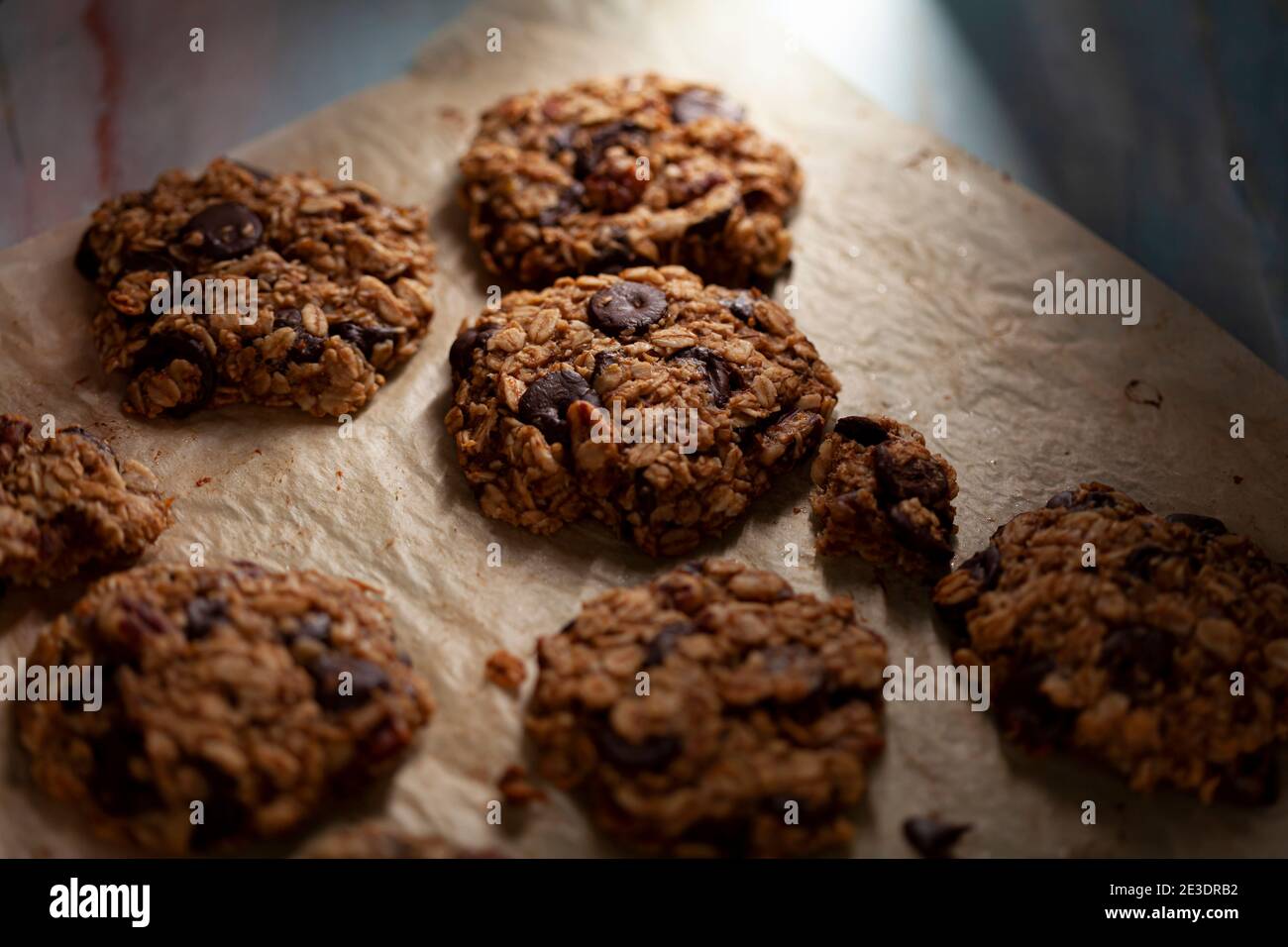 Vista angolata dei biscotti appena fatti sulla carta da forno. Questi sono fatti con avena intera di grano arrotolata con i trucioli di cioccolato scuro. Ci sono pezzi e crumble Foto Stock