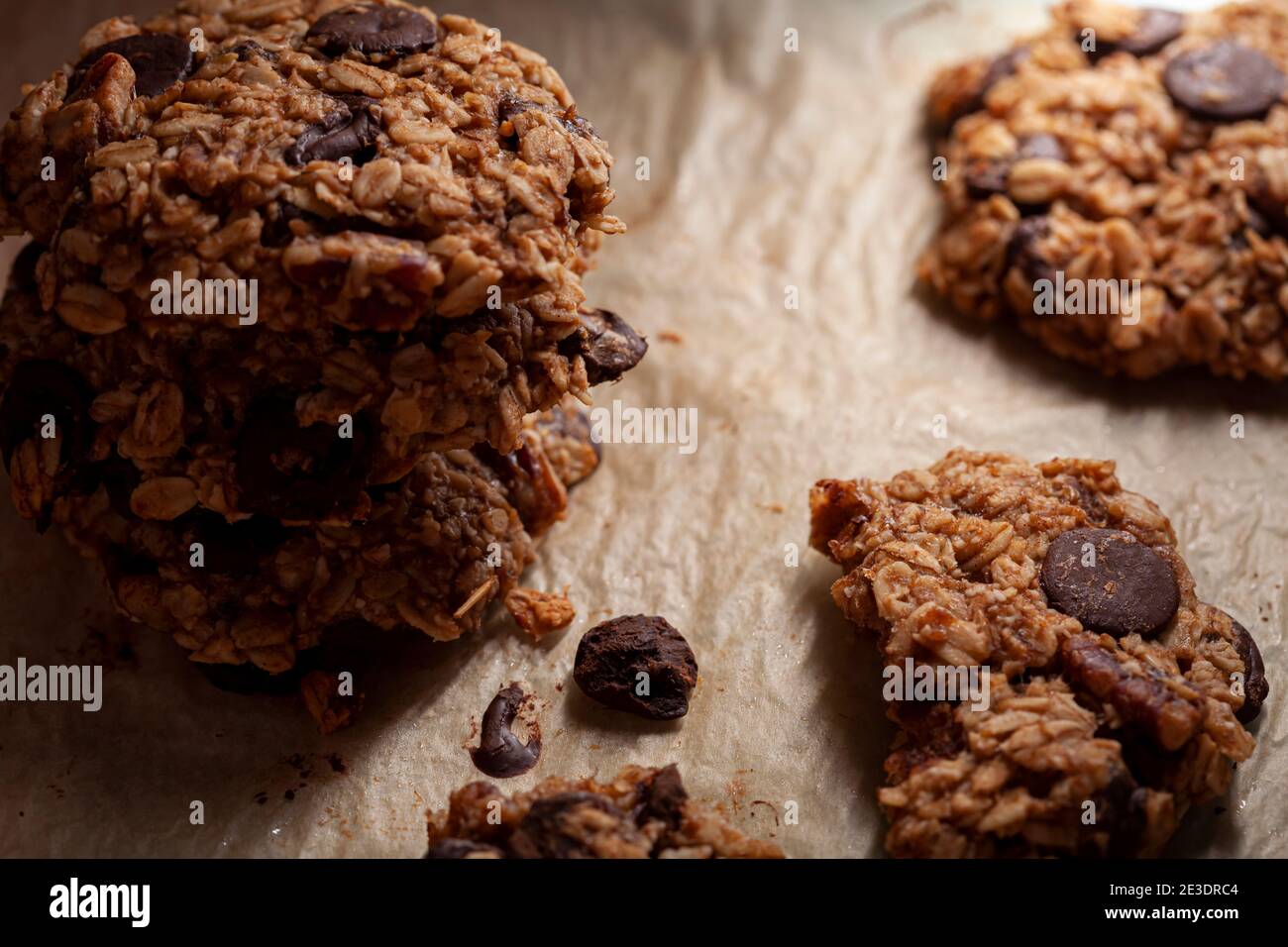 Accatastati biscotti appena fatti su carta da forno. Questi sono fatti con avena intera di grano arrotolata con i trucioli di cioccolato scuro. Ci sono pezzi e crumbles sopra Foto Stock