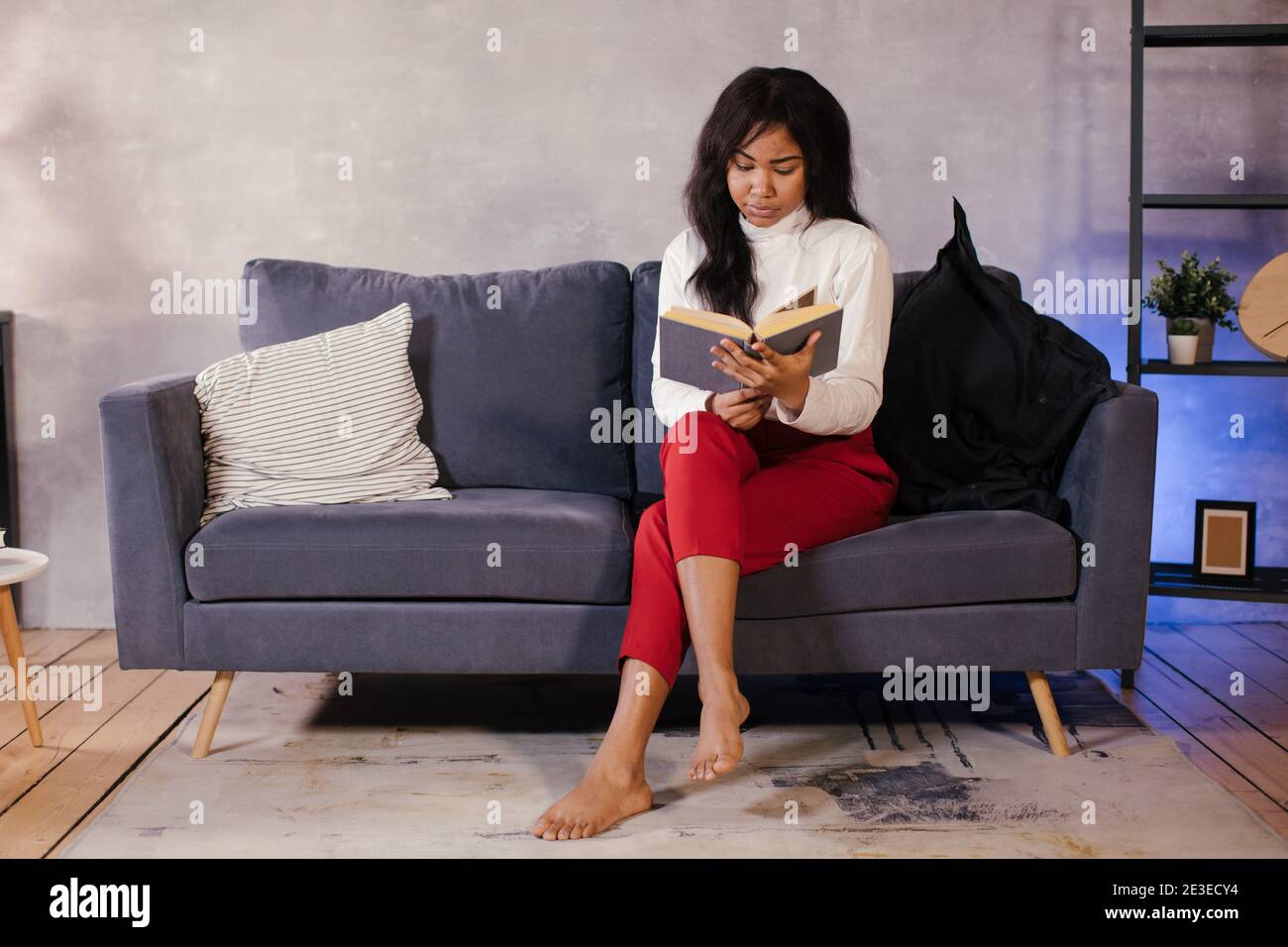 Ragazza africana che legge un libro sul divano in lei camera accogliente Foto Stock