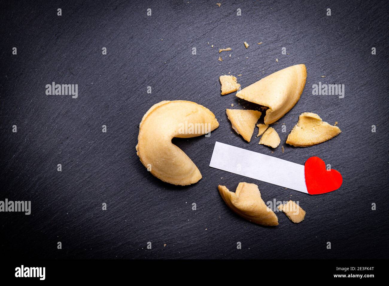 Biscotti Fortune su sfondo di pietra nera con un piccolo cuore rosso. Un cookie rotto rivela un messaggio piacevole. Vuoi leggere il tuo? Foto Stock