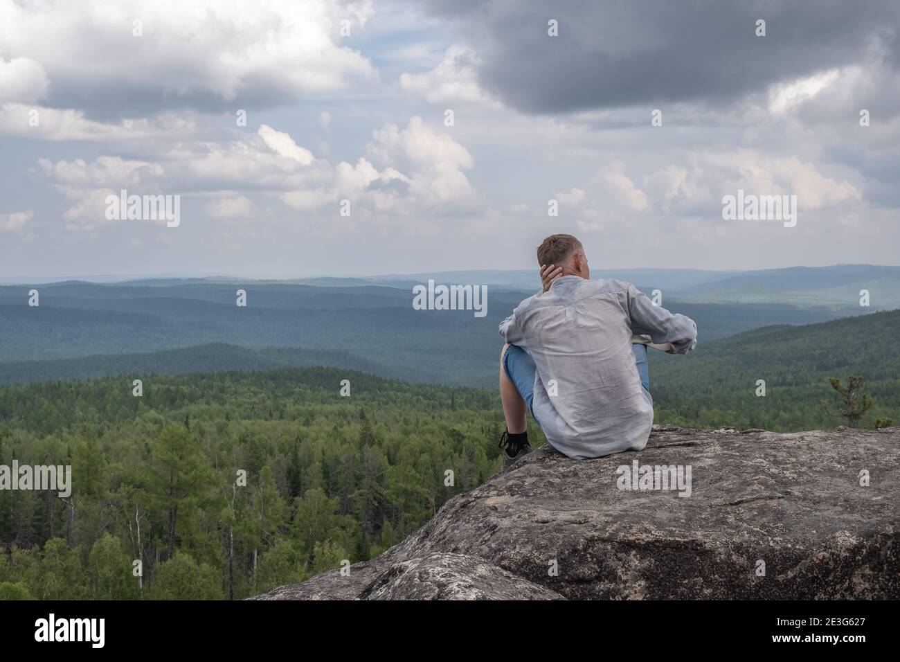 Un uomo libero e di mezza età siede sulla cima di una montagna, ammirando una splendida vista della valle di montagna. Unità con la natura, solitudine. Concetto di viaggio Foto Stock