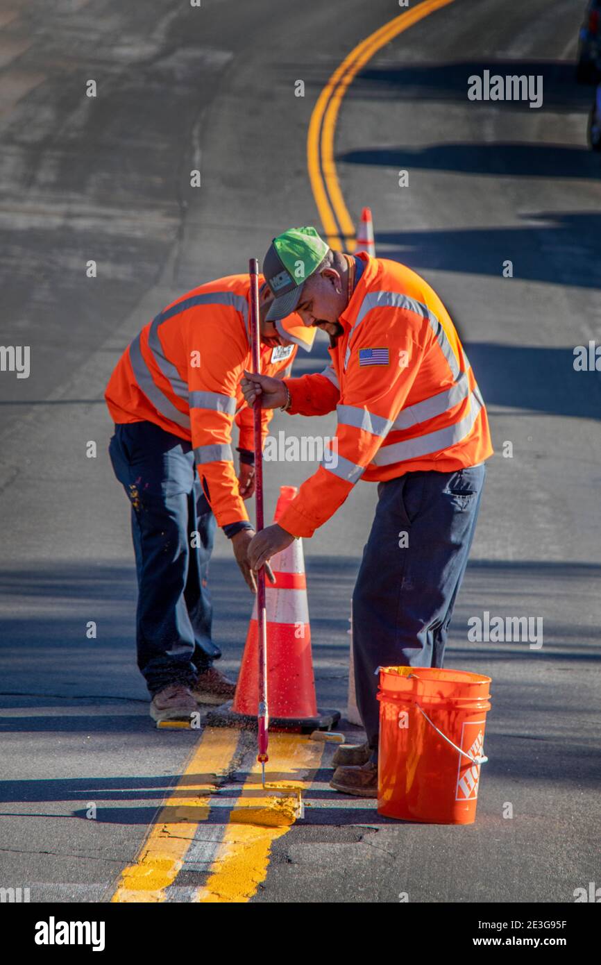 Utilizzando un rullo di vernice giallo, due operai ispanici in giubbotti di sicurezza ripristinare la linea gialla di traffico su una strada a Laguna Niguel, CA. Foto Stock