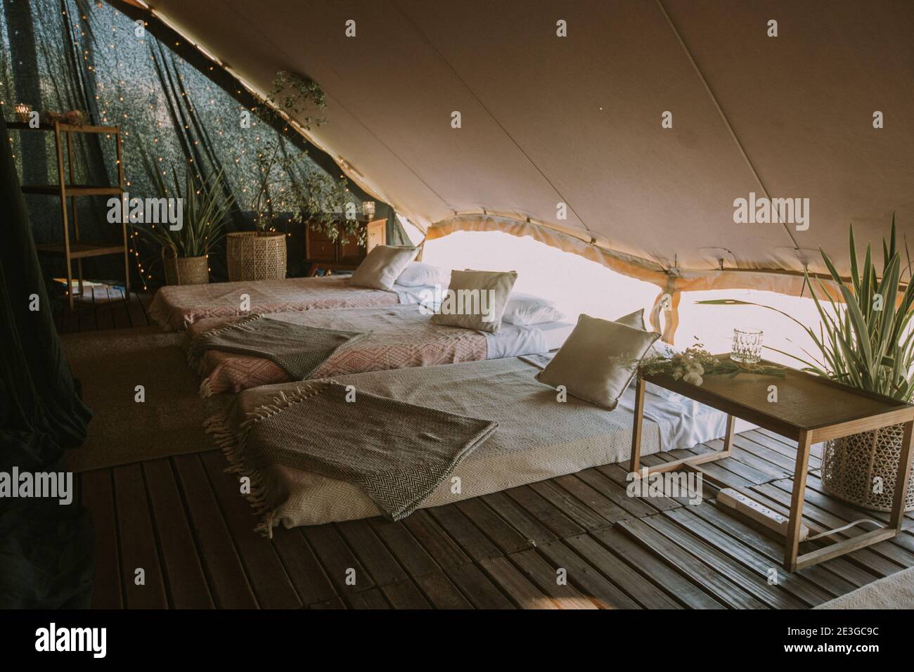 Tenda con 3 materassi, cuscini, tavolo in legno, fiori e luci di fondo. Foto Stock