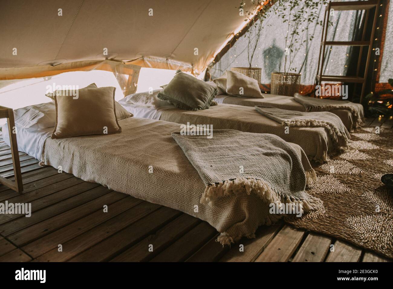 Tenda con 3 materassi, cuscini, tavolo in legno, fiori e luci di fondo. Foto Stock