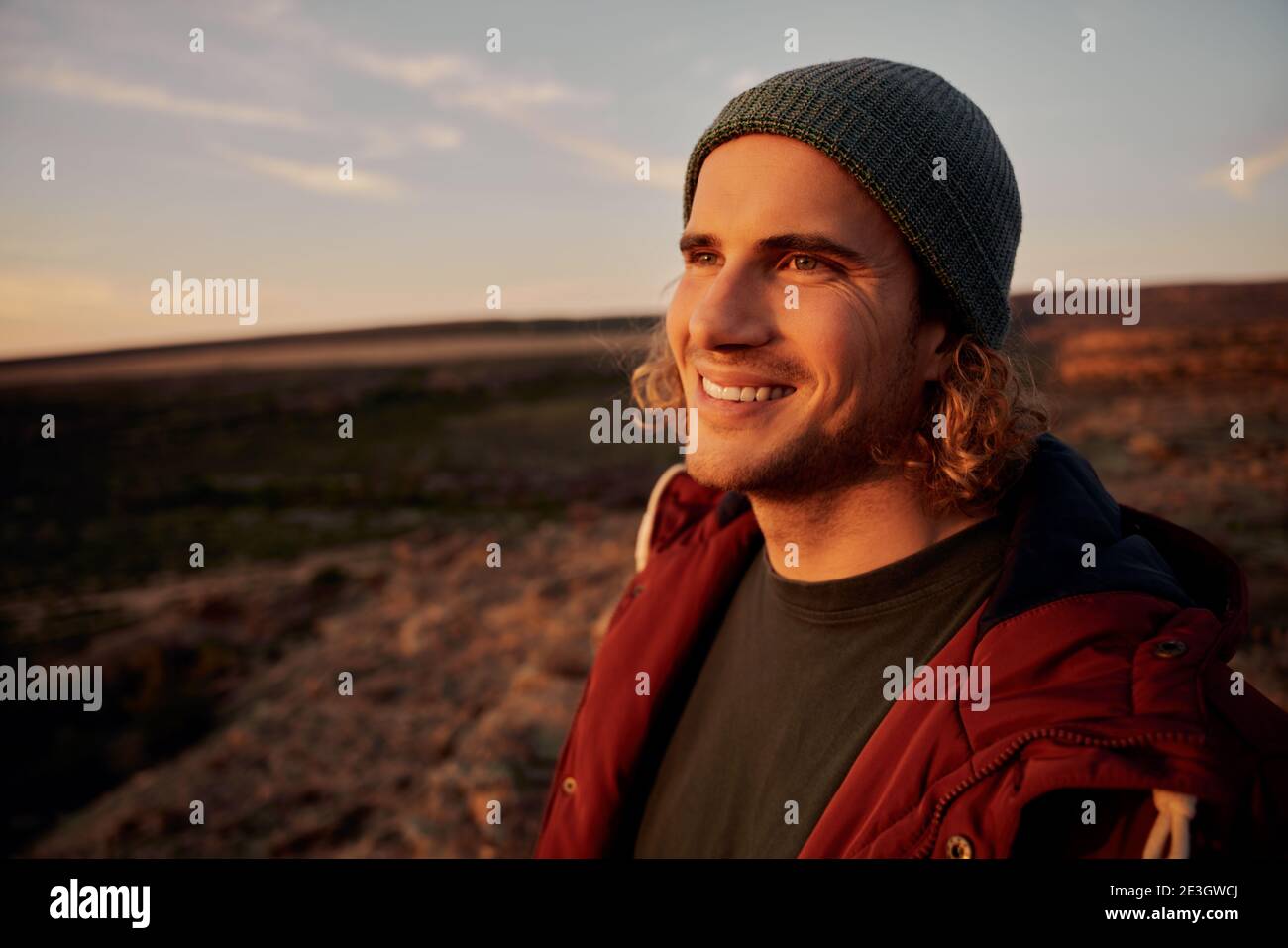 Ritratto di uomo felice indossando il cappuccio sorridente con i raggi solari che cadono in faccia mentre si guarda via Foto Stock