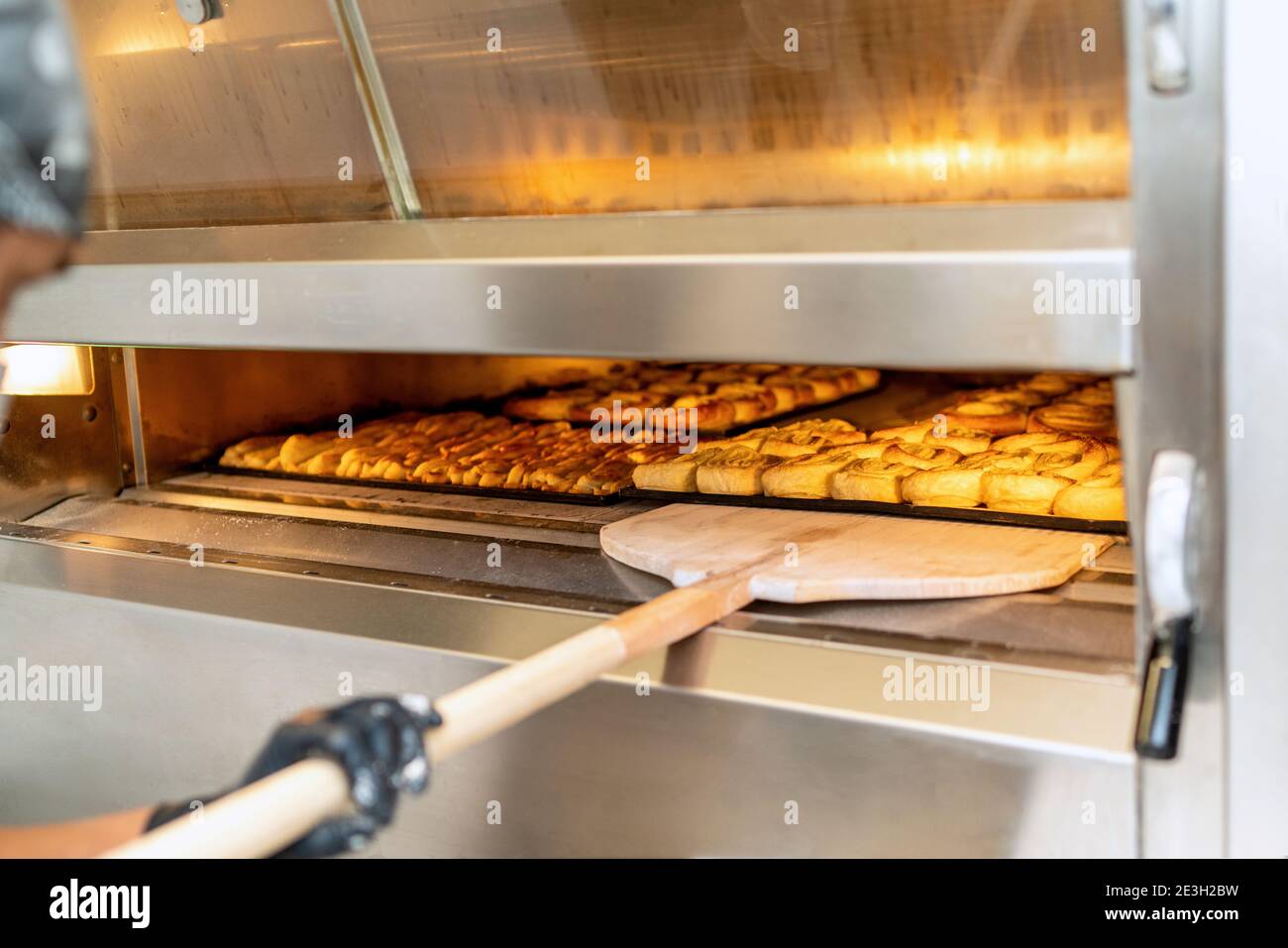 Il panettiere porta un vassoio di torta di riso nel suo mani e lo sta mettendo nel forno della panetteria Foto Stock