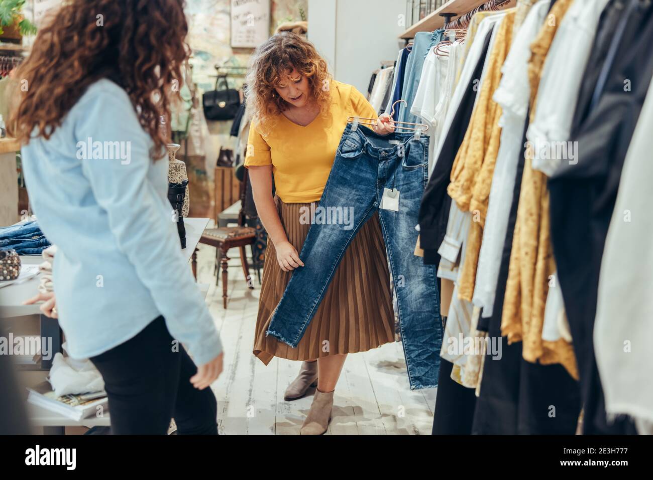 Il proprietario del negozio di moda che mostra un jeans al cliente femminile. Negozio di assistenza per gli acquirenti in negozio di abbigliamento. Foto Stock