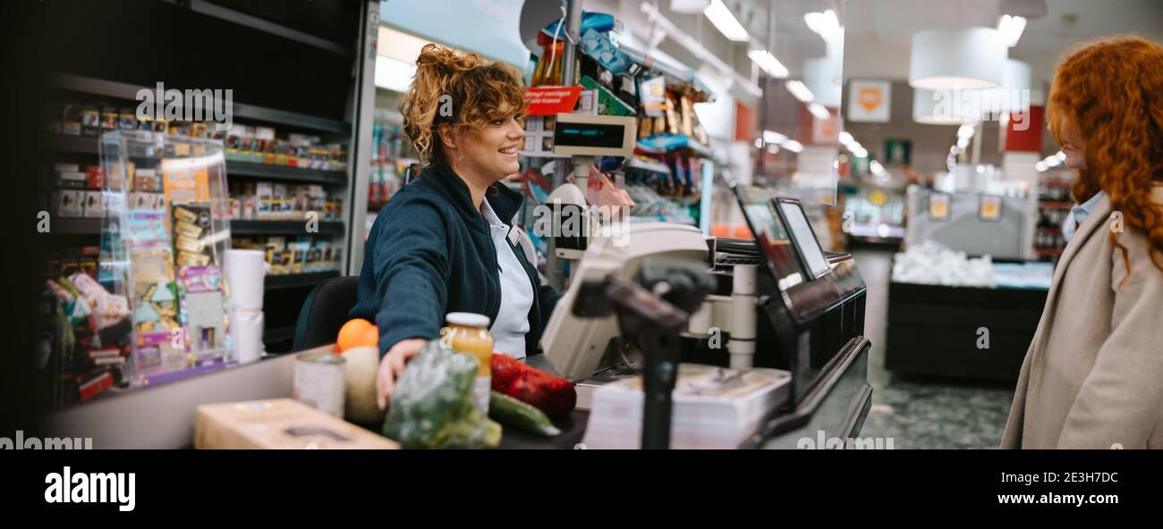 Donna cassiere aiutare cliente donna check out al supermercato. Impiegato del registratore di cassa che assiste l'acquirente al check-out del negozio. Foto Stock
