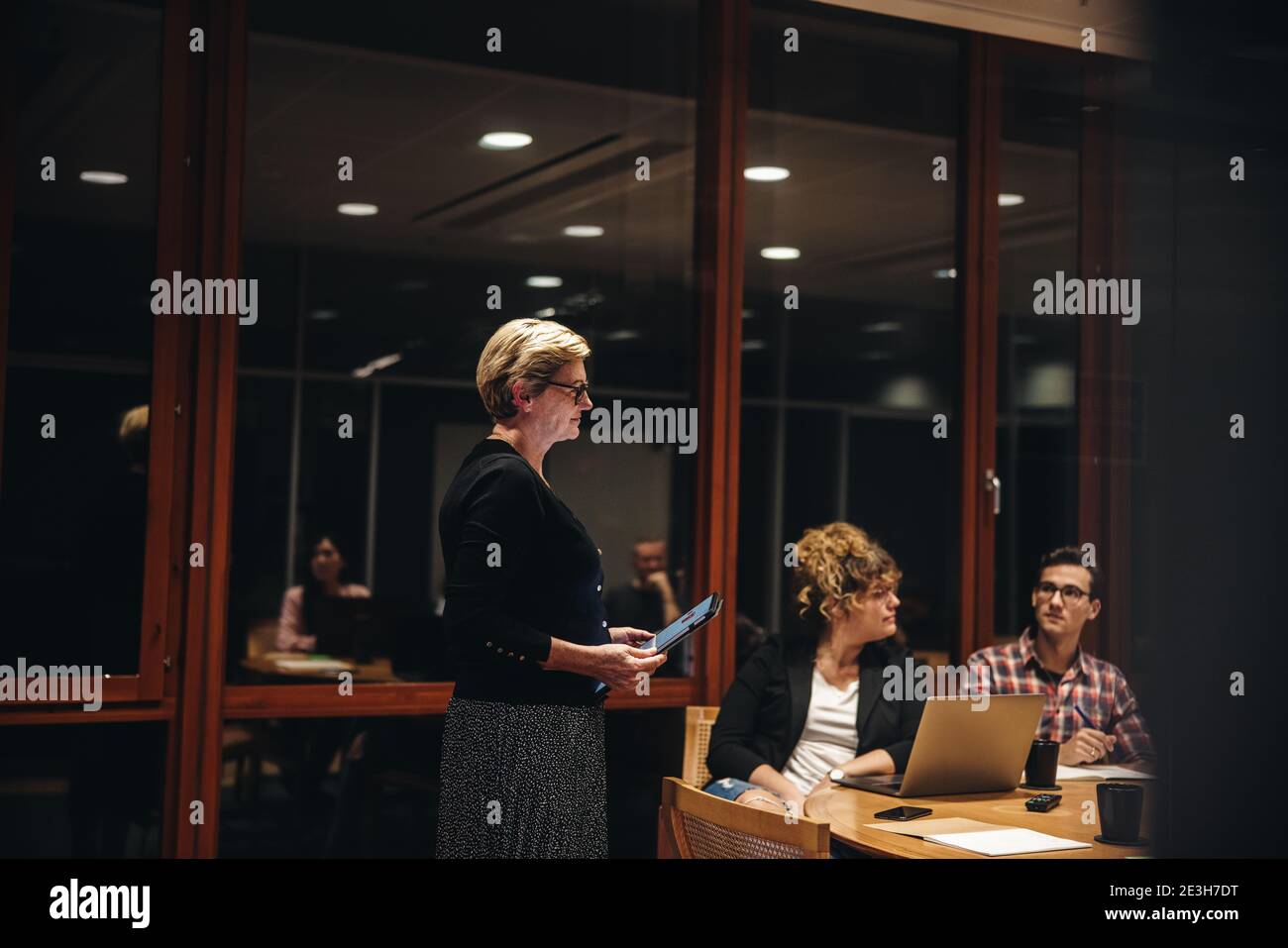 Dirigente donna con tablet digitale che parla con i colleghi nella sala riunioni. professionisti che si occupano di riunioni notturne nella sala riunioni. Foto Stock