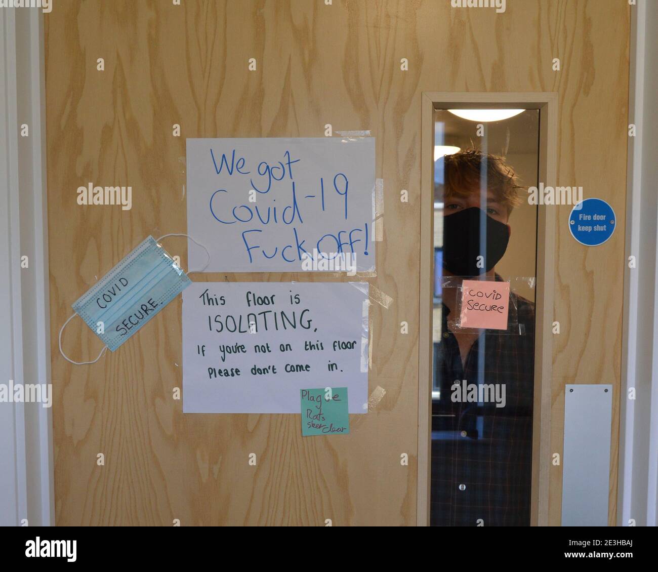 Uno studente universitario guarda attraverso il vetro su una porta come il loro intero piano auto isolato nei loro appartamenti studenti a Cheltenham come il Regno Unito continua a sopportare la pandemia di Coronavirus. Foto Stock