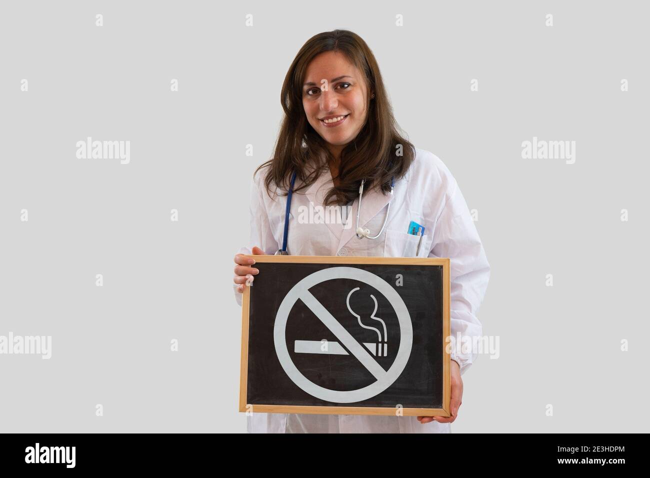 Sorridente dottoressa che tiene la lavagna con divieto di fumare. Smettere di fumare concetto. Isolato su sfondo grigio. Foto Stock