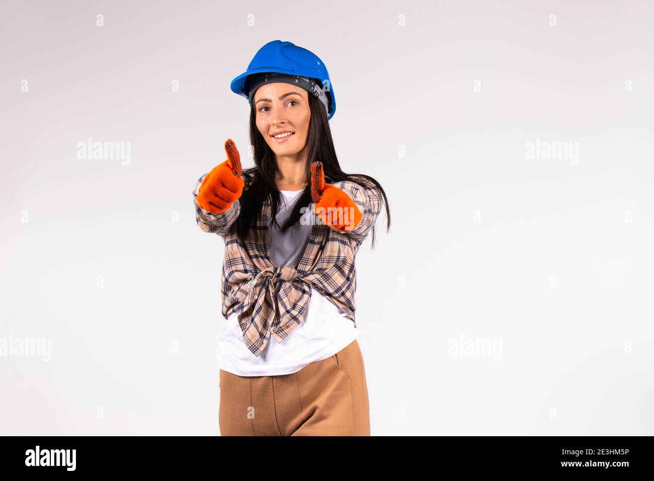 Sorridente meccanico donna in un casco e guanti mostra la classe alla fotocamera. Sfondo bianco con spazio vuoto. Foto Stock