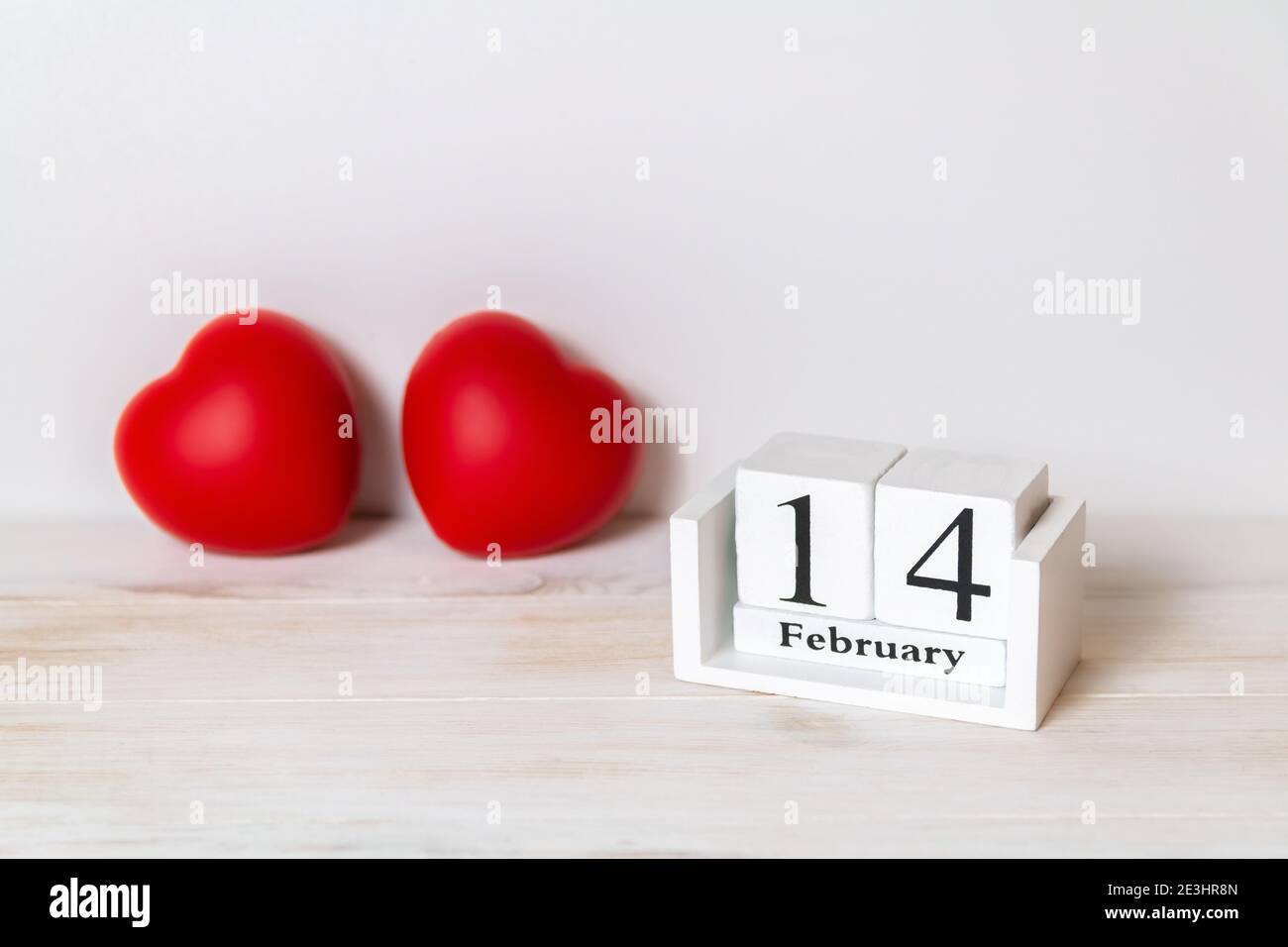 Calendario in legno che mostra il 14 febbraio e cuori rossi dietro di esso. San Valentino. Spazio di copia. Messa a fuoco selettiva Foto Stock