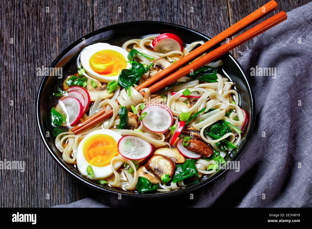 Zuppa di noodle di Udon - zuppa calda giapponese in un recipiente nero con chosticks in brodo marrone con spinaci saltati, rafano, uova sode e soffici, funghi a fette Foto Stock