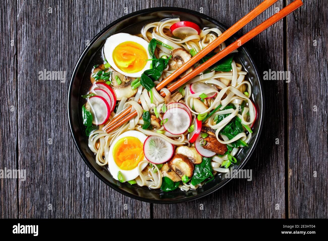 Zuppa di noodle di Udon - zuppa calda giapponese in un recipiente nero con chosticks in brodo marrone con spinaci saltati, rafano, uova sode e soffici, funghi a fette Foto Stock
