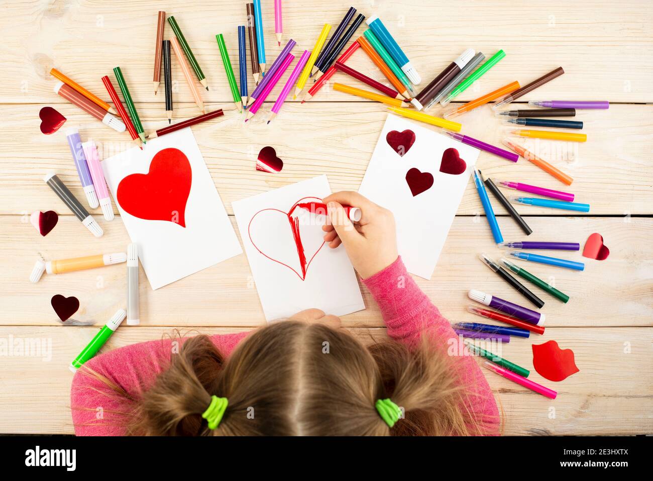 La bambina prepara le carte con i cuori per San Valentino. Il disegno e  l'applicazione vengono eseguiti dal bambino utilizzando matite colorate o  penne a punta di feltro. Chi Foto stock 