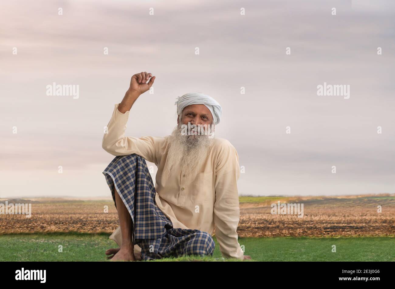 UN VECCHIO VILLAGGIO TURBANED UOMO SEDUTO SU TERRENI AGRICOLI E FELICEMENTE PENSARE Foto Stock