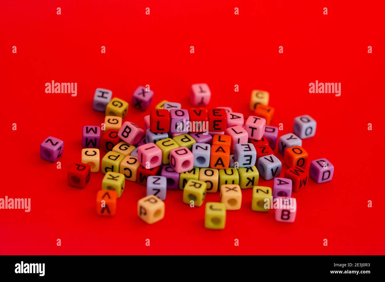 Perle colorate di legno cubico con lettere su sfondo rosso festivo, parola 'amore'. San Valentino. 14 di febbraio. Disposizione piatta, vista dall'alto. Foto Stock