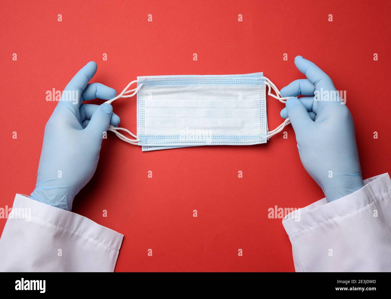 due mani maschili in guanti di lattice blu tengono un medico maschera monouso su sfondo rosso Foto Stock