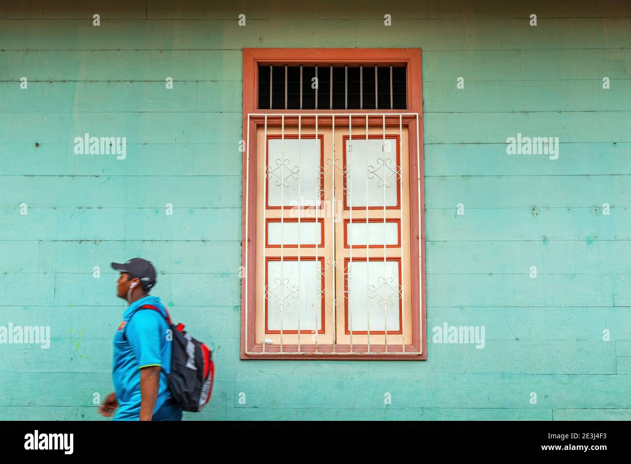 Giovane ecuadoriano con auricolari che passano per l'architettura coloniale finestra a Guayaquil, Ecuador. Foto Stock