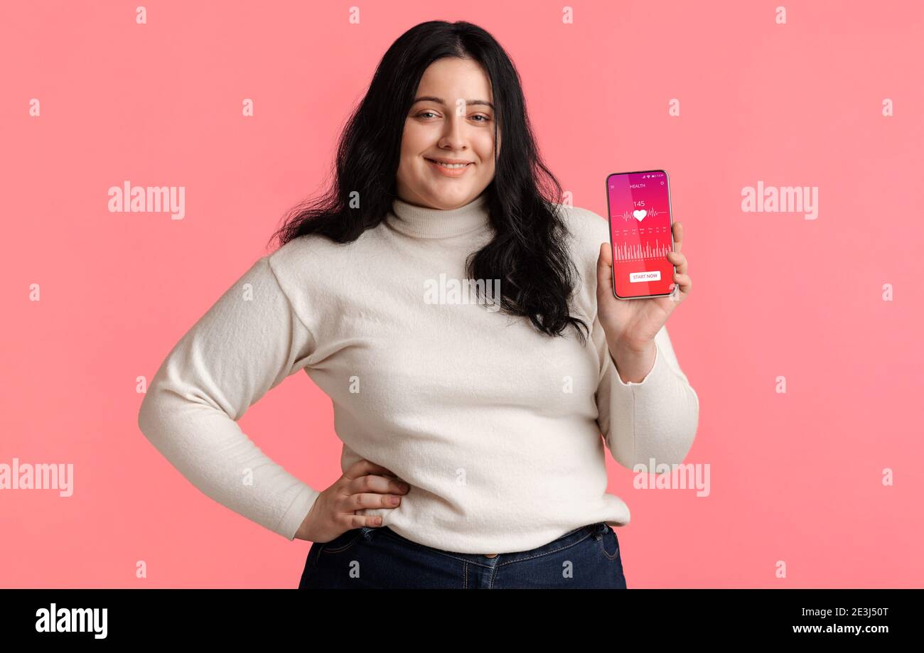 Plus-Size Donna che mostra telefono con Cardio Tracker applicazione, sfondo rosa Foto Stock