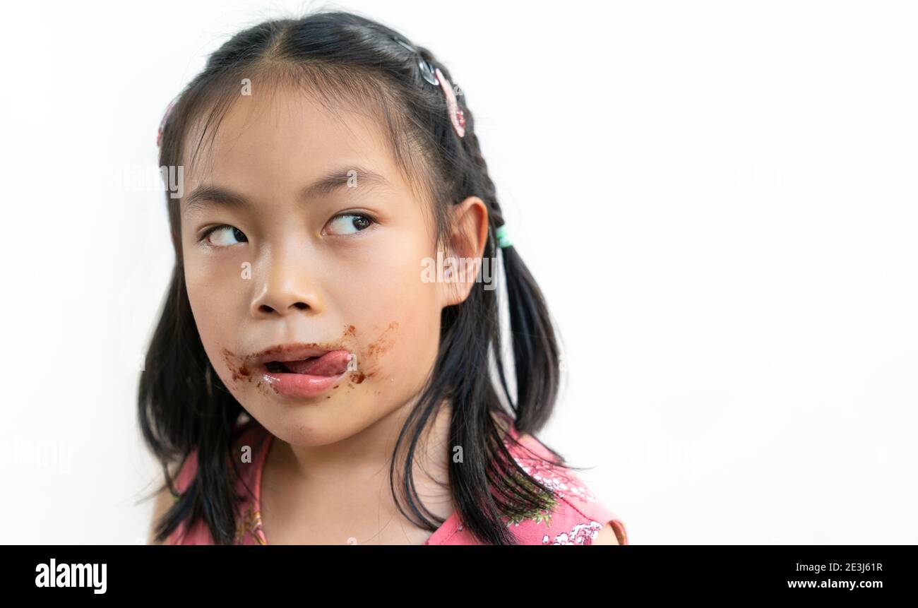 Primo piano su faccia di ragazza bambino cute asiatica con sudicio di cioccolato intorno alla sua bocca, guardare a spazio vuoto sul lato per la copia, i prodotti o il disegno, la lingua Foto Stock