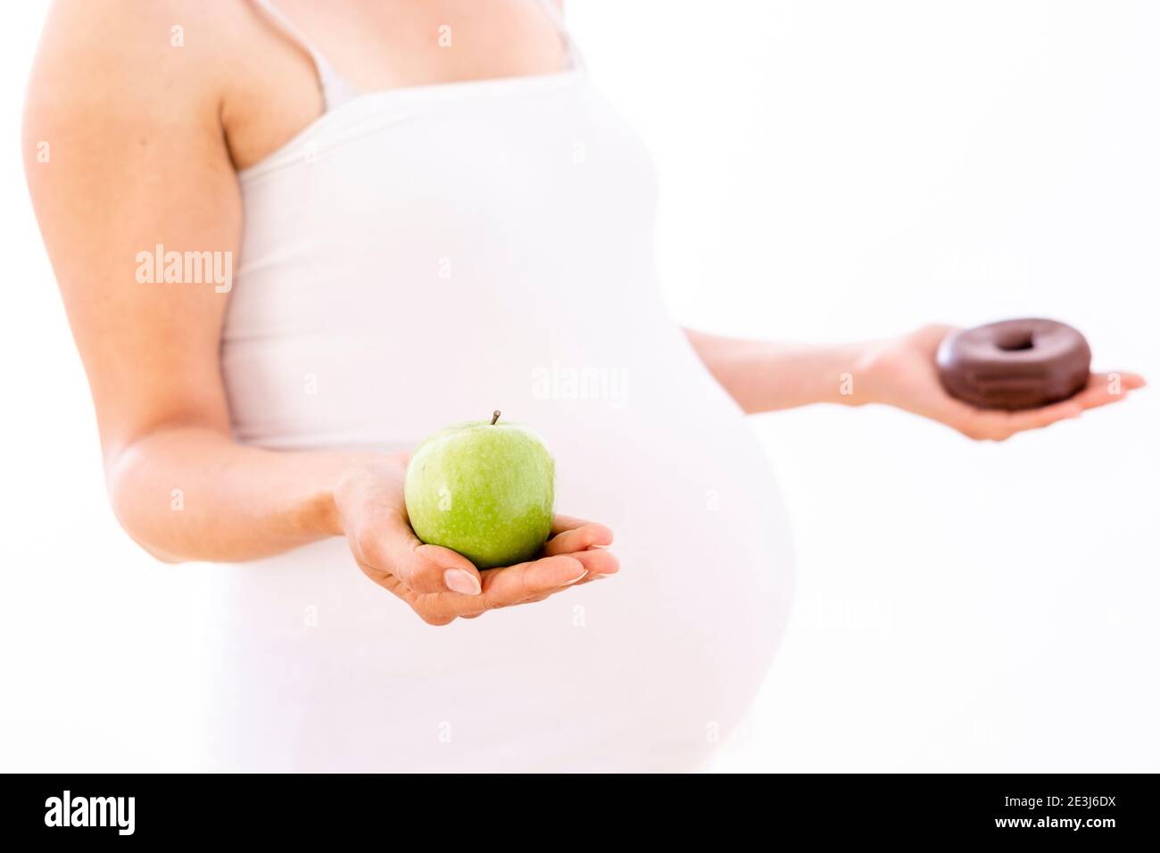 Donna incinta che sceglie la mela sana sopra la ciambella malsana su bianco sfondo Foto Stock