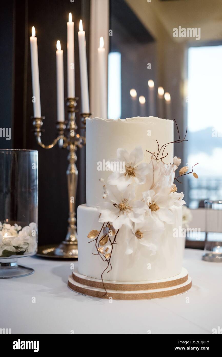 Torta di nozze bianca decorata con fiori e candele nel sfondo Foto Stock